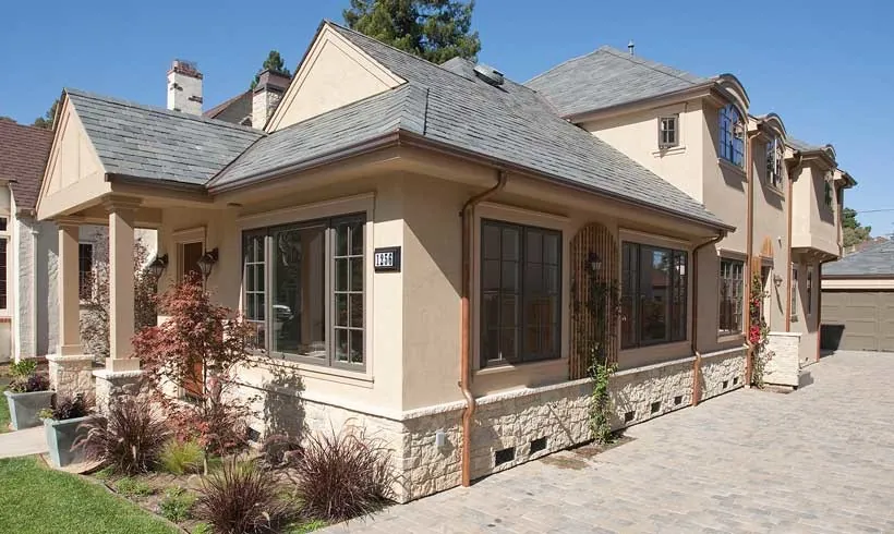 Side of a Burlingame residence with beige stucco, a stone base, a slate roof, and a paver driveway.