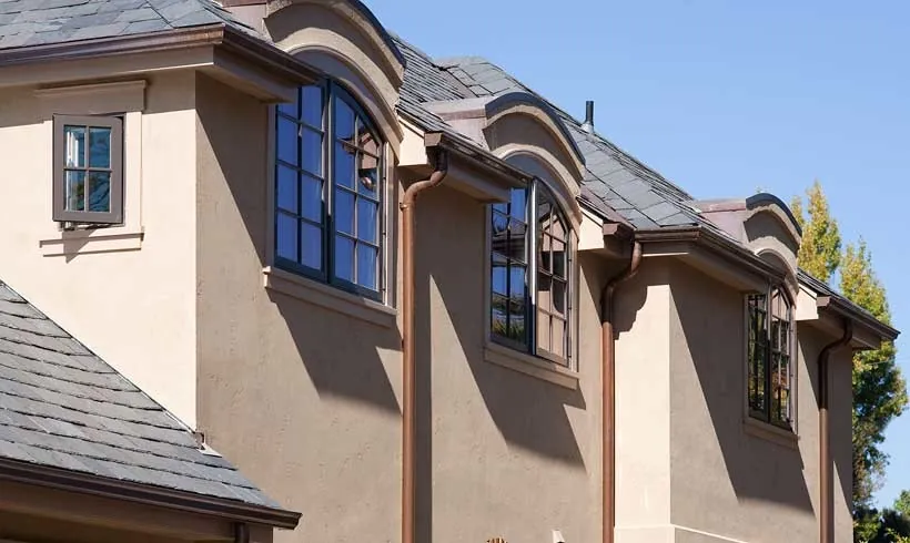 Upper story of a Burlingame residence with beige stucco, a slate roof, and arched divided-light windows.