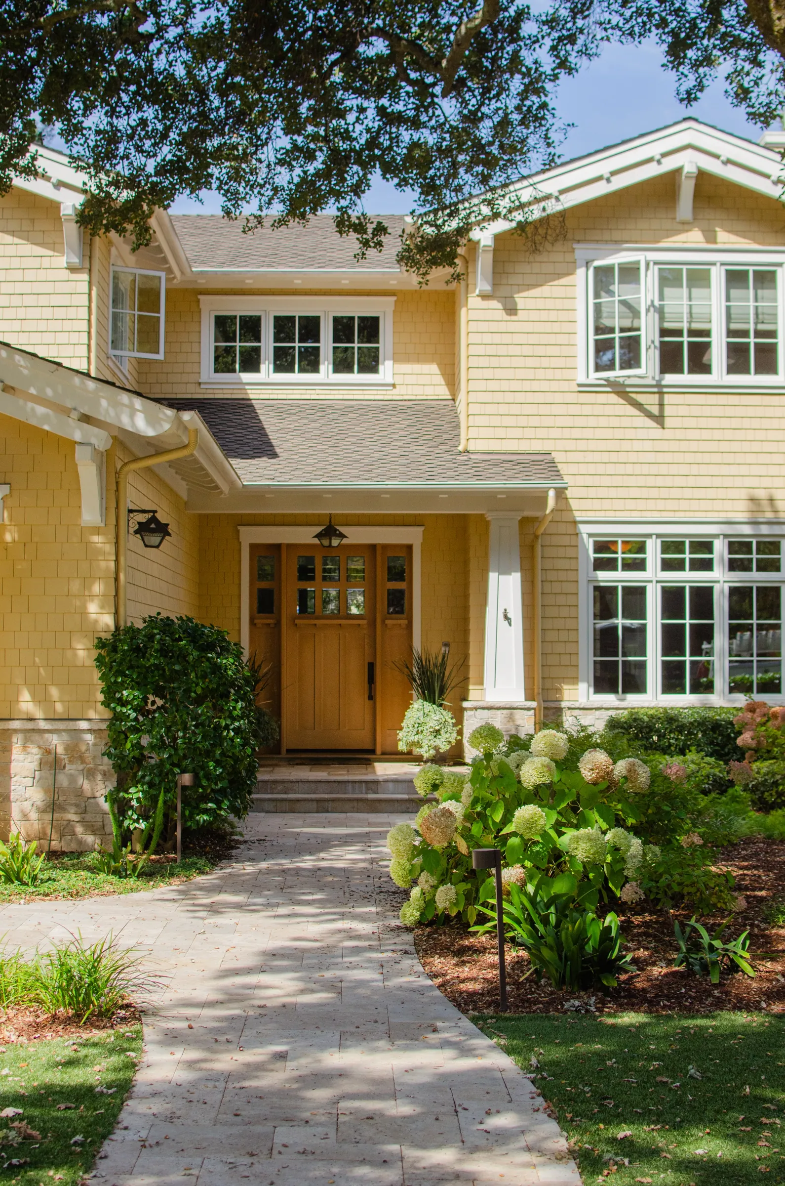 Front entry of a Menlo Park residence with yellow shingle siding, white trim, and a wood door under a covered entry.