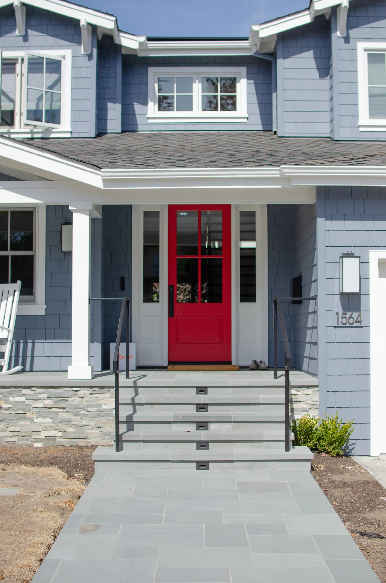 Closer view of a San Carlos entry with blue shingle siding, a red door, stone steps, and black metal railings.