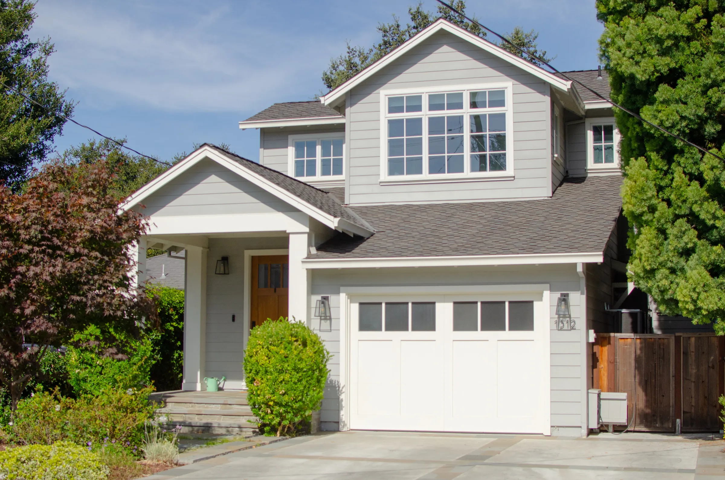 Front of a San Carlos residence with gray siding, white trim, a gabled upper story, a covered entry, and a white garage door.
