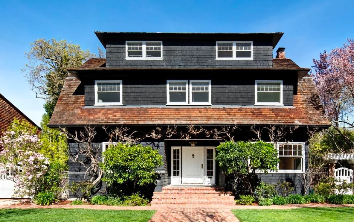 Shingle-style exterior with a cedar roof, white divided-light windows, and a brick front walk.